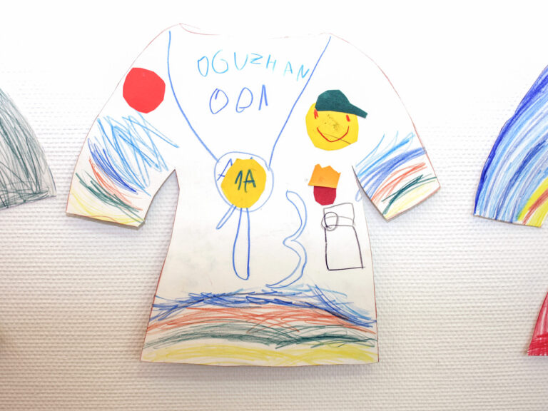 Umriss eines T-Shirt aus Karton, der von einem Kind bemalt und mit Tonpapier beklebt wurde